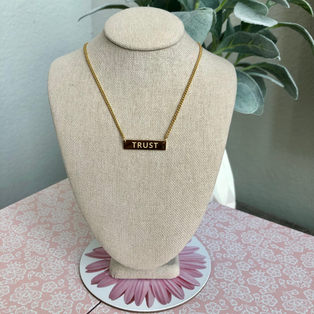 Gold plated necklace with the word trust engraved on bar.