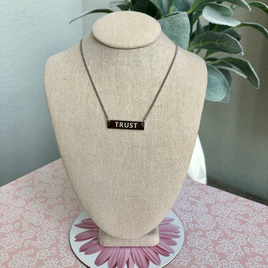 Silver necklace with the word trust engraved on bar.